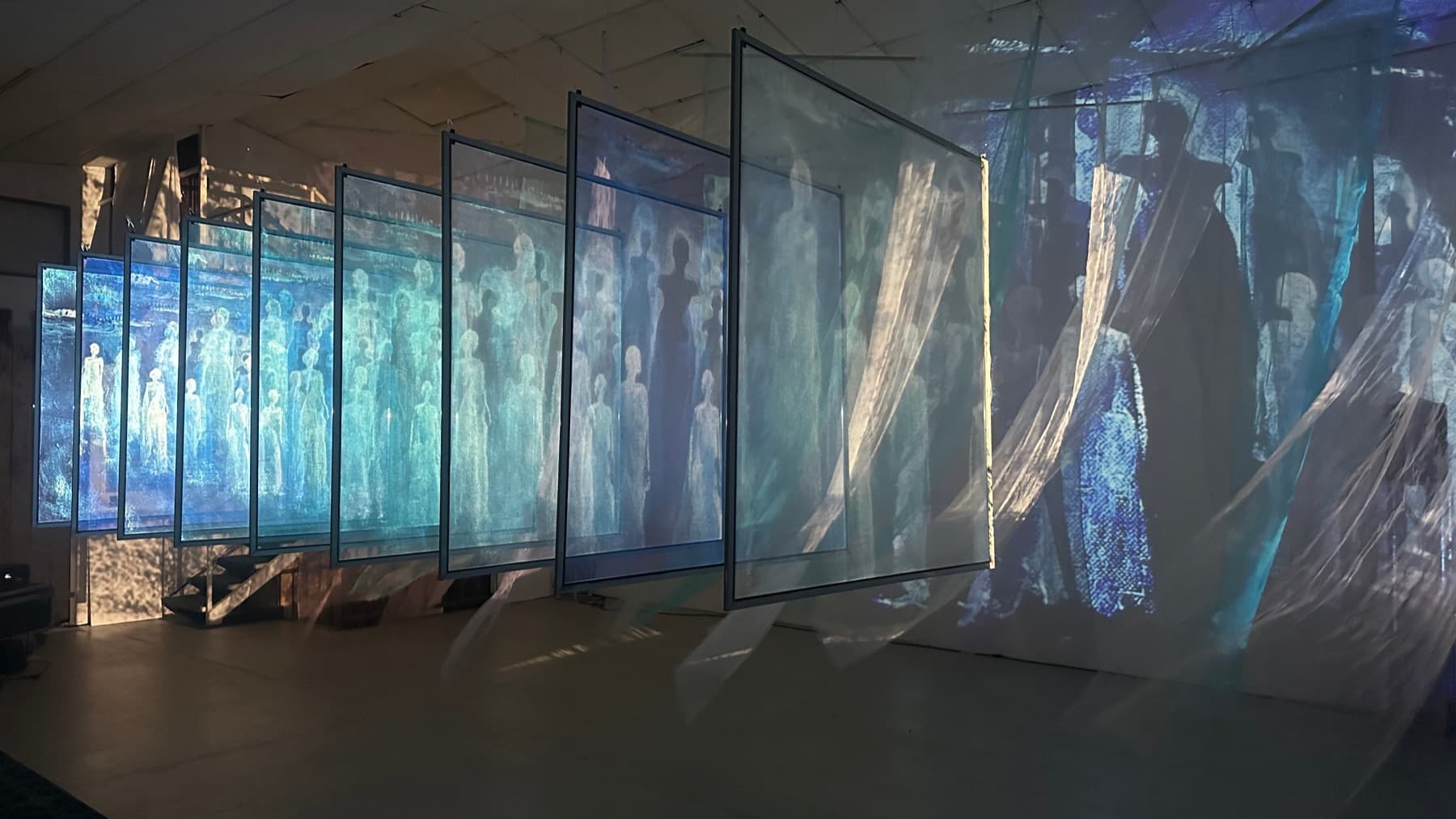 Hanging tulle screens with blue projected figures at the Tūhono installation